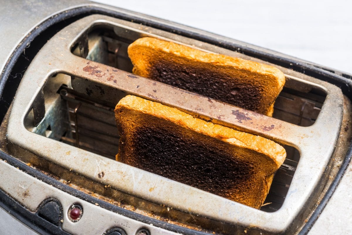又脏又旧的烤面包机，白色的木质背景上有烧焦的烤过头的面包。坏的，有缺陷的厨房电器。bd手机下载