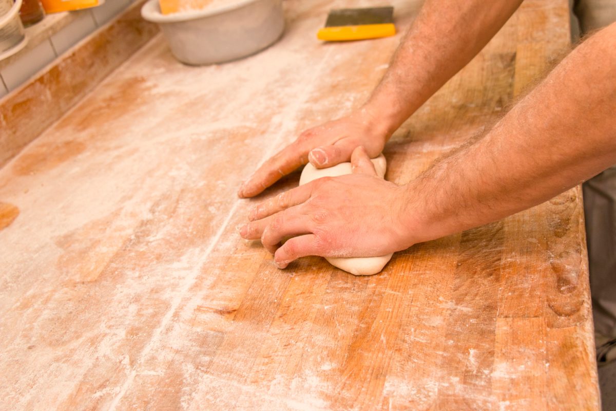 一个面包师的手揉面包面团洒在面粉工作台上