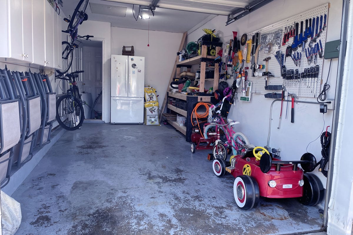 一个狭窄的车库内部，有很多存储的工具，自行车零件，后面有一个冰箱