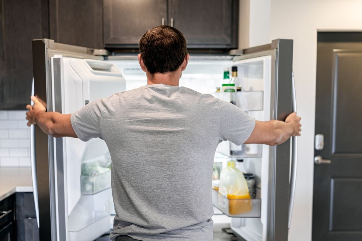 饥饿的男人打开冰箱门，家用电器在现代厨房里用调味品和果汁寻找食物bd手机下载
