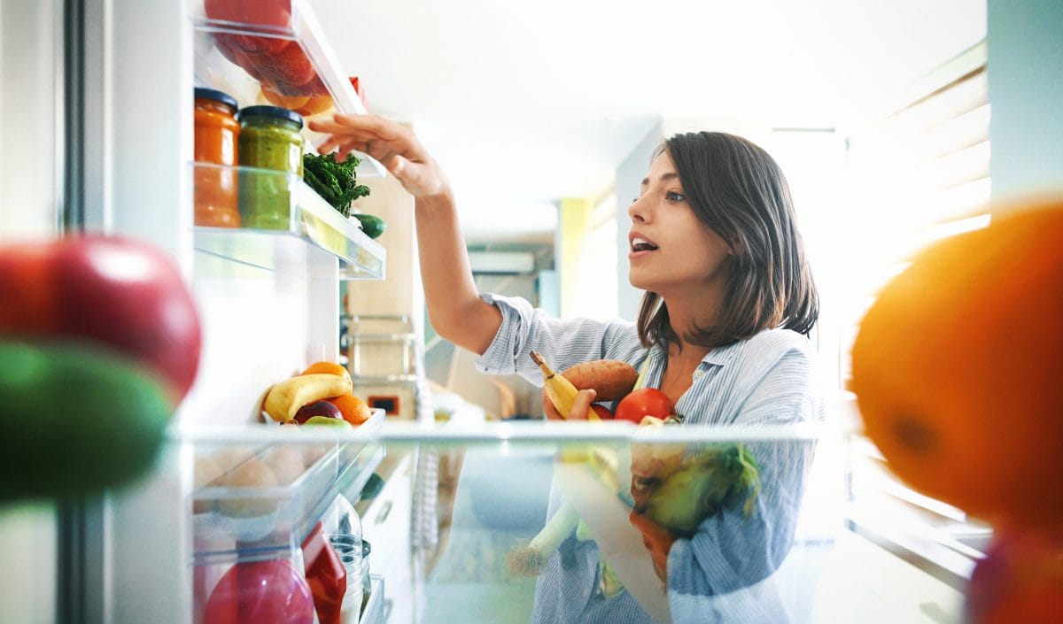 周日早上，一对快乐的年轻夫妇从冰箱里挑选一些水果和蔬菜，做一些健康的早餐。从冰箱里拍的。