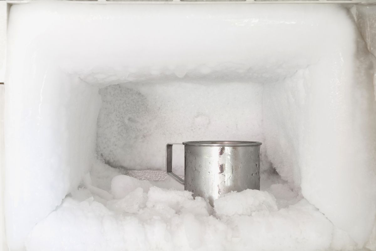 冰箱冷冻室不锈钢饮水杯。冰柜墙壁内的冰堆积。