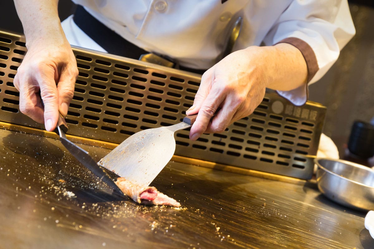 日本铁板烧厨师在一个宽敞的煎锅上煎肉片