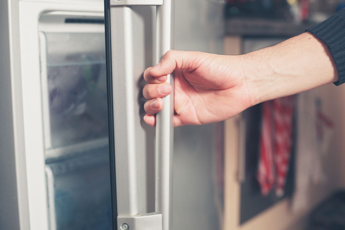近距离照片，一名男子手握冰箱把手，打开冰箱门