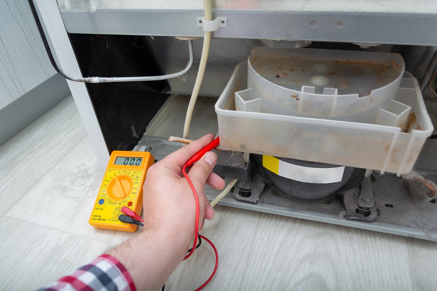 男技术员用数字万用表检查冰箱。修理冰箱和家用电器的承包商