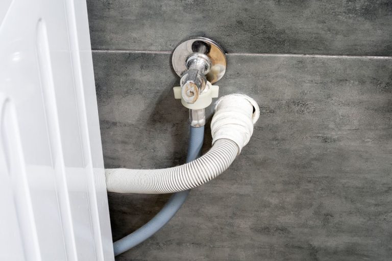 肮脏的下水道和水软管的洗衣机运行到墙上覆盖着灰色的混凝土砖。设计选项在一个舒适的现代浴室。——为洗碗机钻孔排水软管吗?