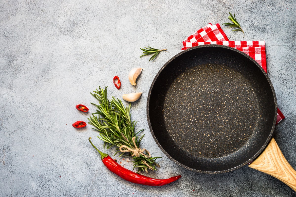 食物烹饪背景与煎锅或平底锅，香料和香草在灰色石桌上