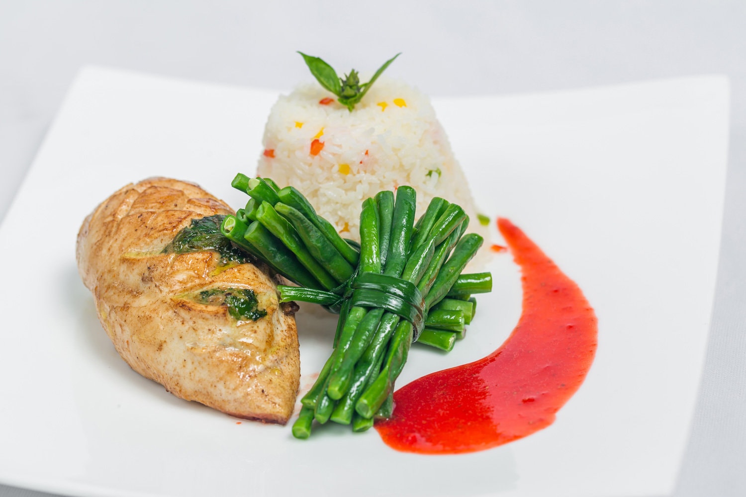平底锅烤鸡胸肉配长青豆和清淡蔬菜米饭拼盘。白色盘子上用红酱装饰的食物。孤立的白色背景。