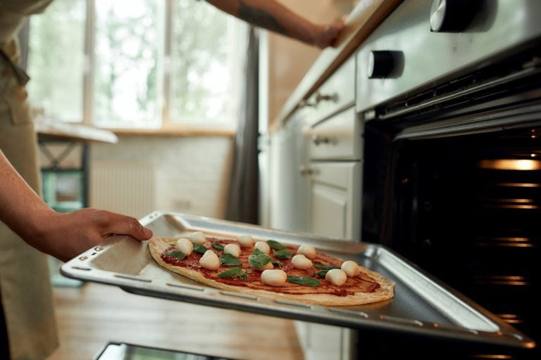 出现的人,专业的厨师在家里做匹萨。人在围裙把生在现代烤箱烤披萨。爱好,生活方式。有选择性的重点。侧视图。网页横幅,比萨饼烤箱可以多靠近房子吗?