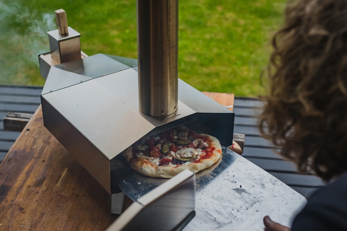 一名男子正在从一个用颗粒燃料的不锈钢家用便携式烤箱中取出美味的新鲜自制披萨。