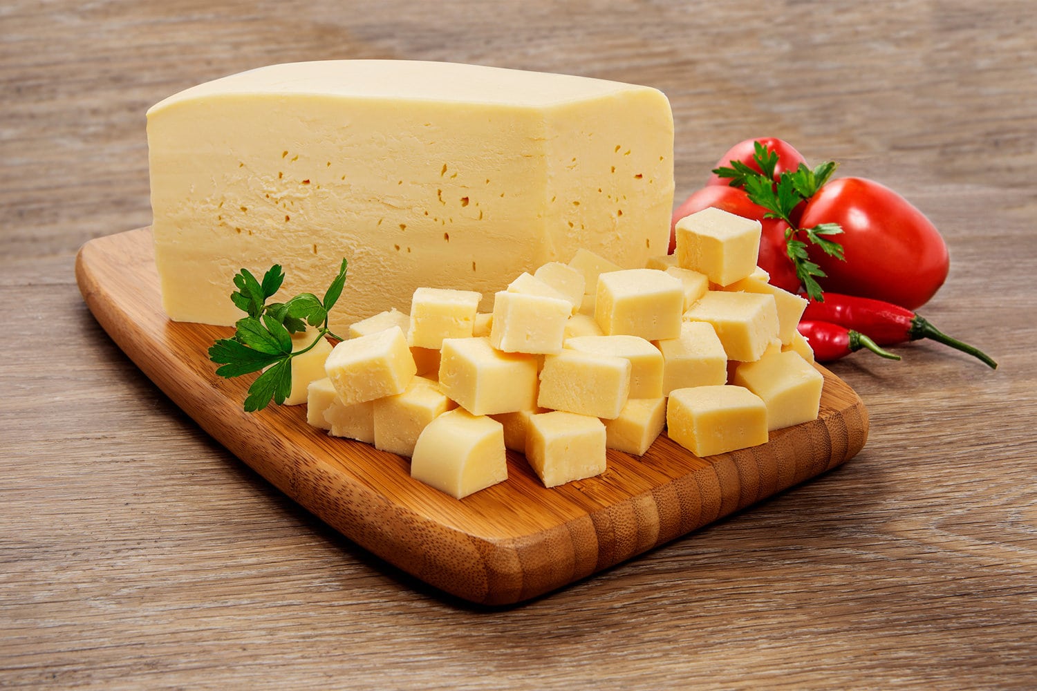 Mozzarella cheese in pieces and cut into cubes on wooden cutting board on wooden background.