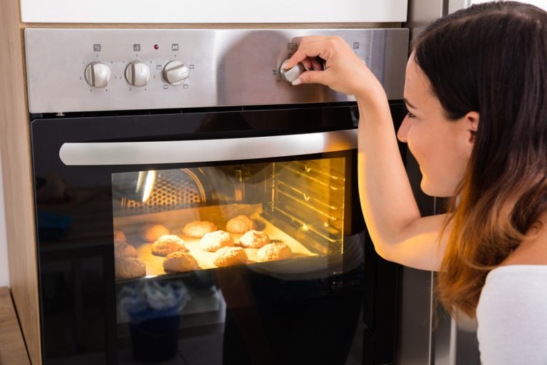 年轻女子使用微波炉在厨房烤新鲜的饼干,烤箱要热在外面吗?bd手机下载