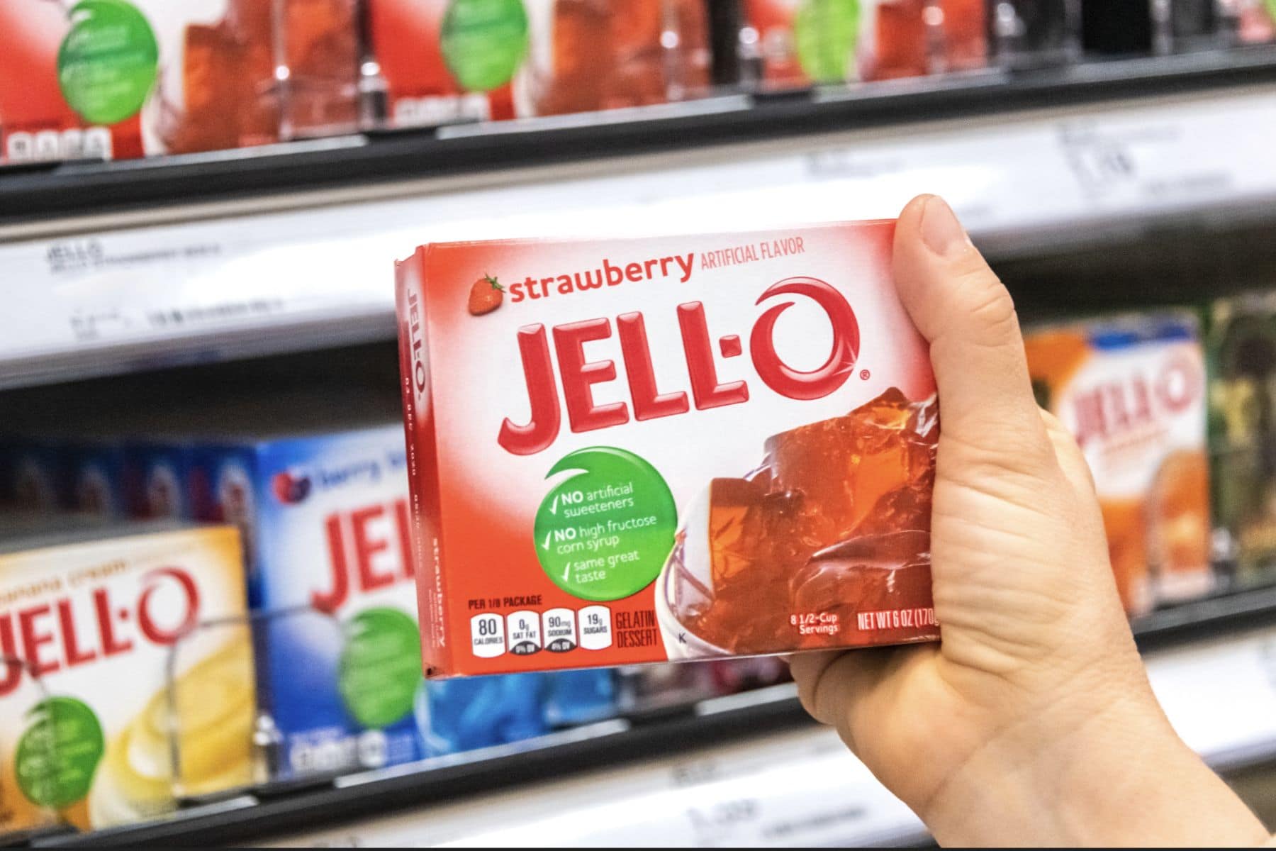 在超市的货架上，购物者手拿一盒果冻草莓明胶甜点