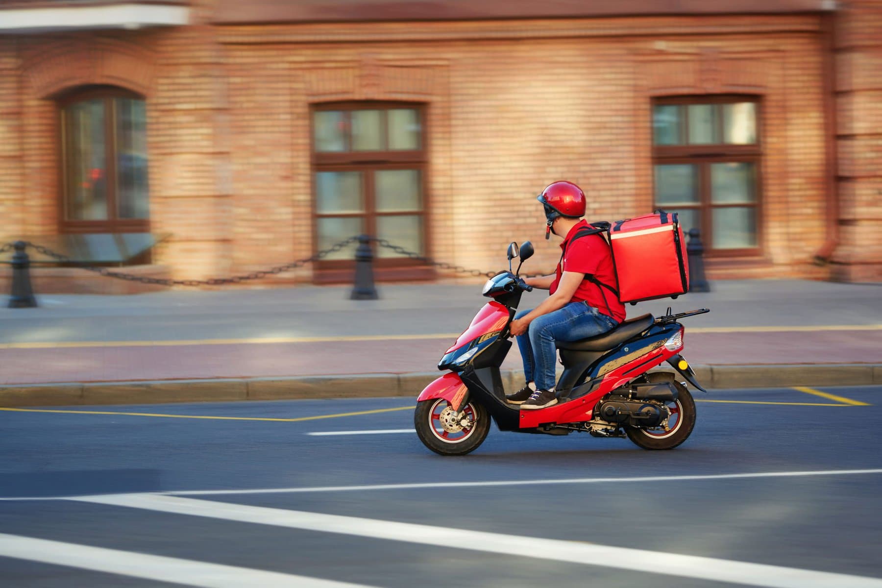 外卖小哥骑着恒温食品箱的滑板车快速行驶。咖啡馆和餐厅的快速送餐服务。骑摩托车送餐的快递员。