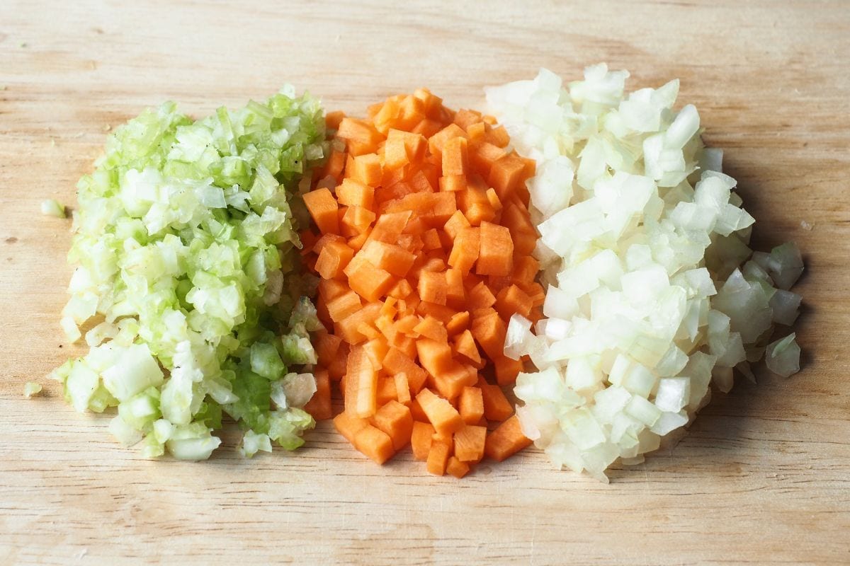 将芹菜、胡萝卜和洋葱切碎，放在木砧板上。