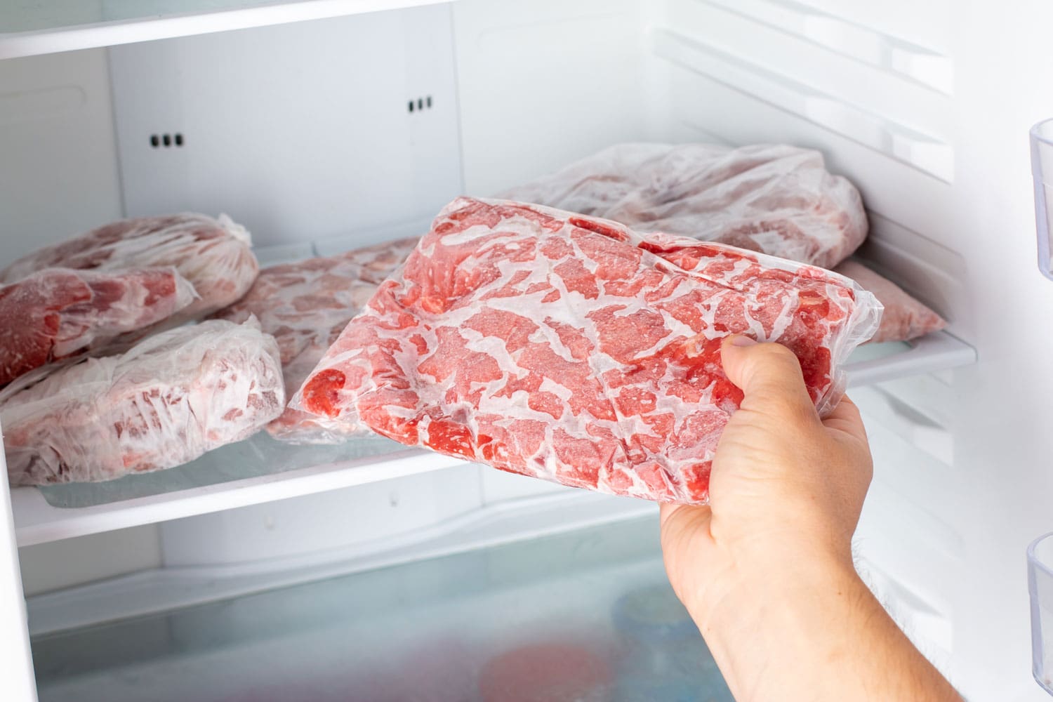 男人从家里厨房的冰箱里拿出一袋冻肉。bd手机下载冷冻食品