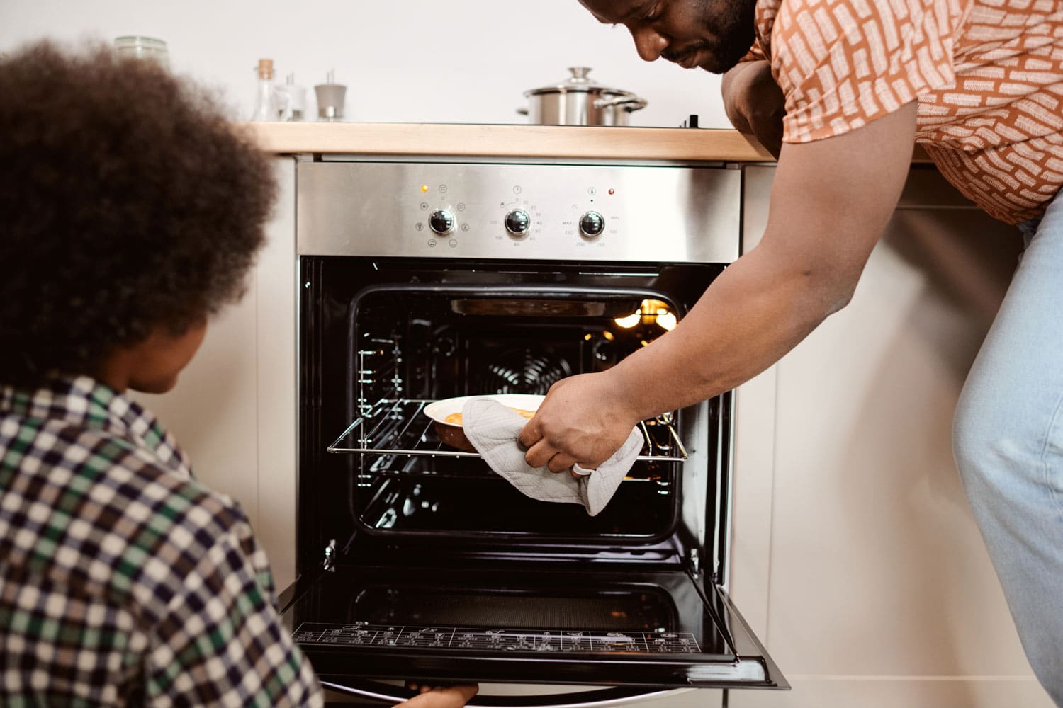 年轻的非洲男子在他的小儿子面前从电烤箱里拿出热苹果派