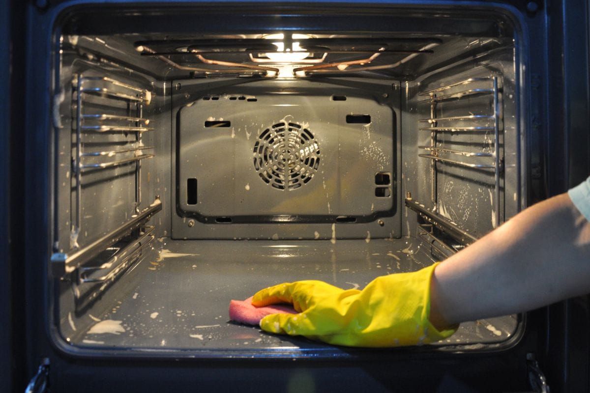 清洁烤箱在厨房里。bd手机下载在一个黄色的家用手套的重点放在烤箱的背景。