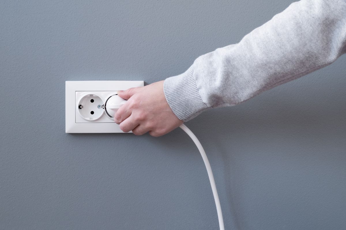 手插入电线到白色塑料插座或欧洲灰色石膏墙墙上的插座。仔细的观察一个女人的手将电插头插入墙上的插座。