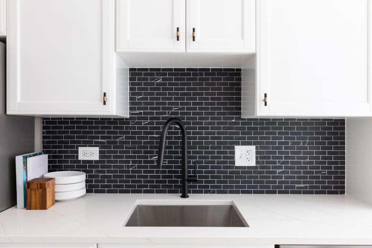 bd手机下载厨房水槽的细节拍摄与白色橱柜、小黑色大理石的地铁瓷砖连壁,和一个黑色的水龙头。