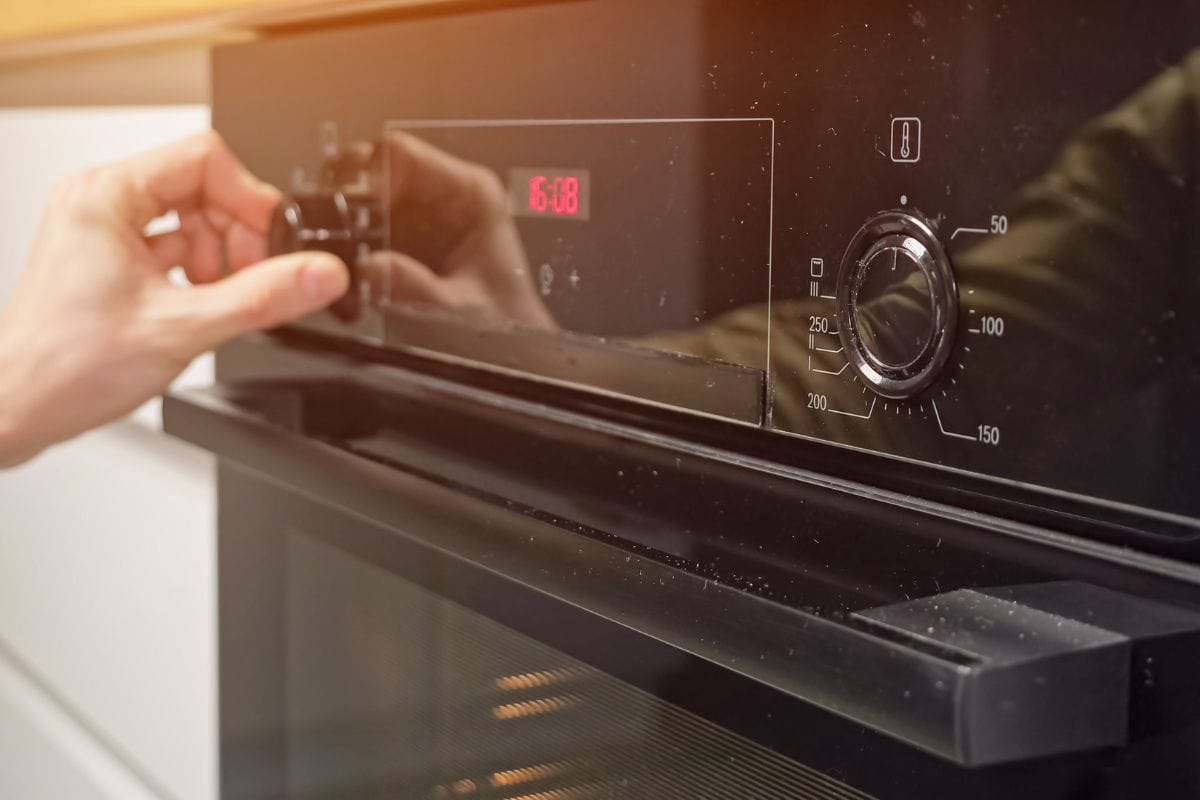 人调整温度和设置操作模式在现代厨房的烤箱。bd手机下载管家准备晚餐使用在家烹饪用具,阳光。